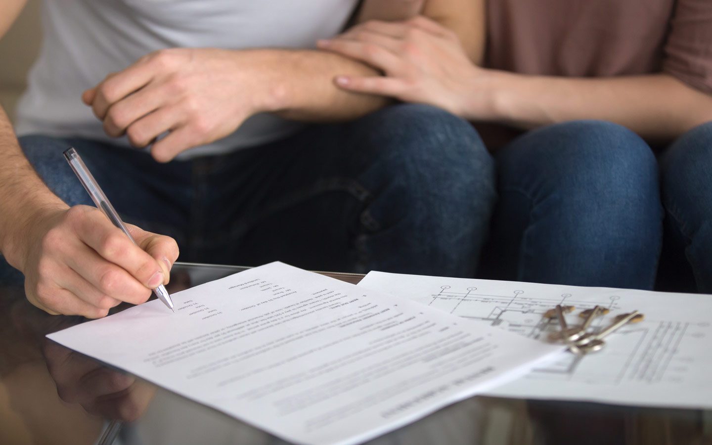 Auckland couple signing home loan documents with their mortgage broker, new house keys on the table